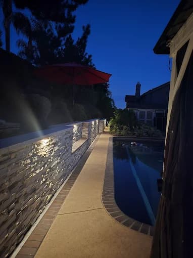 Backyard pool and stone retaining wall illuminated by outdoor lighting at night